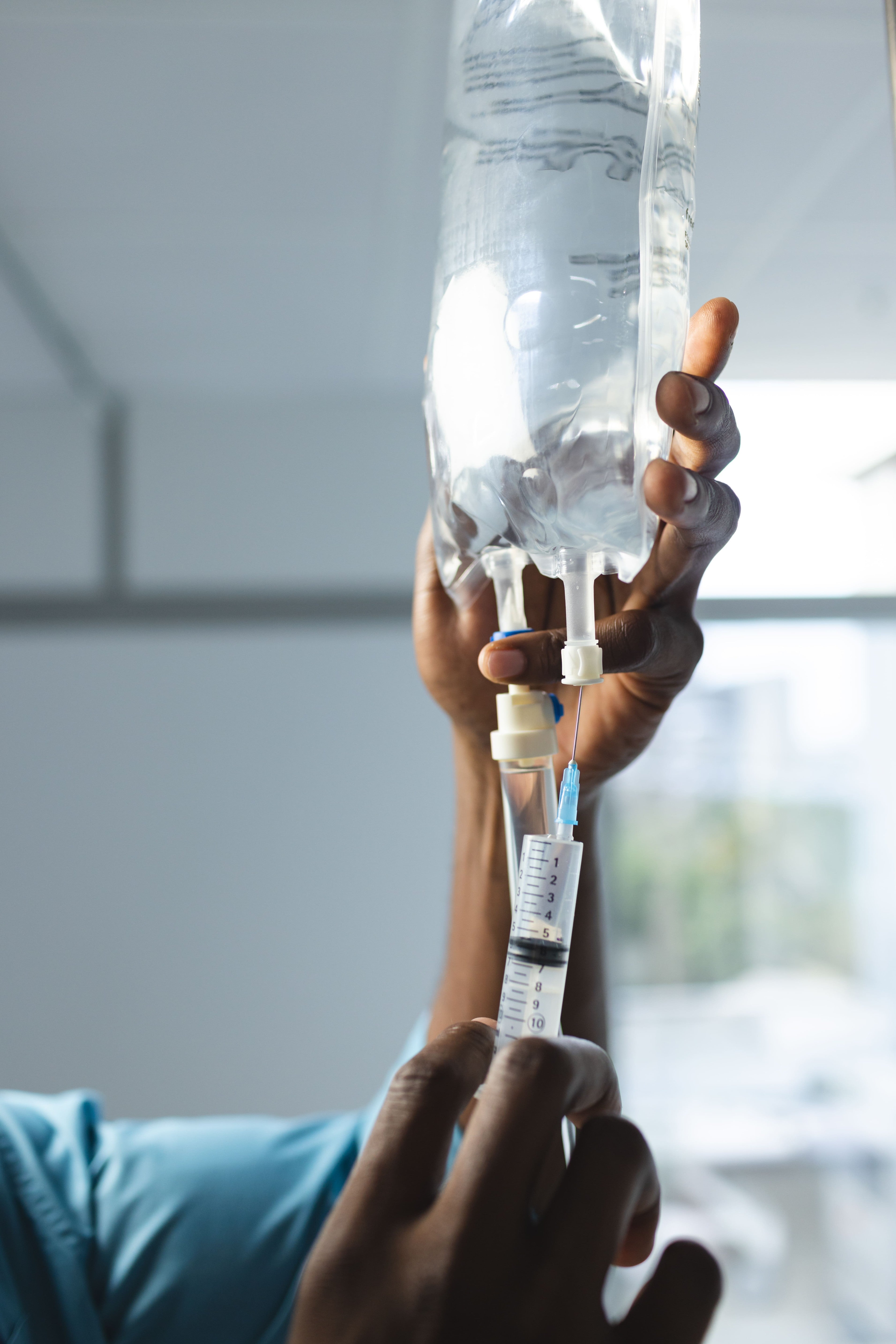 Nurse preparing IV fluid drip with syringe for patient care and fluid balance management