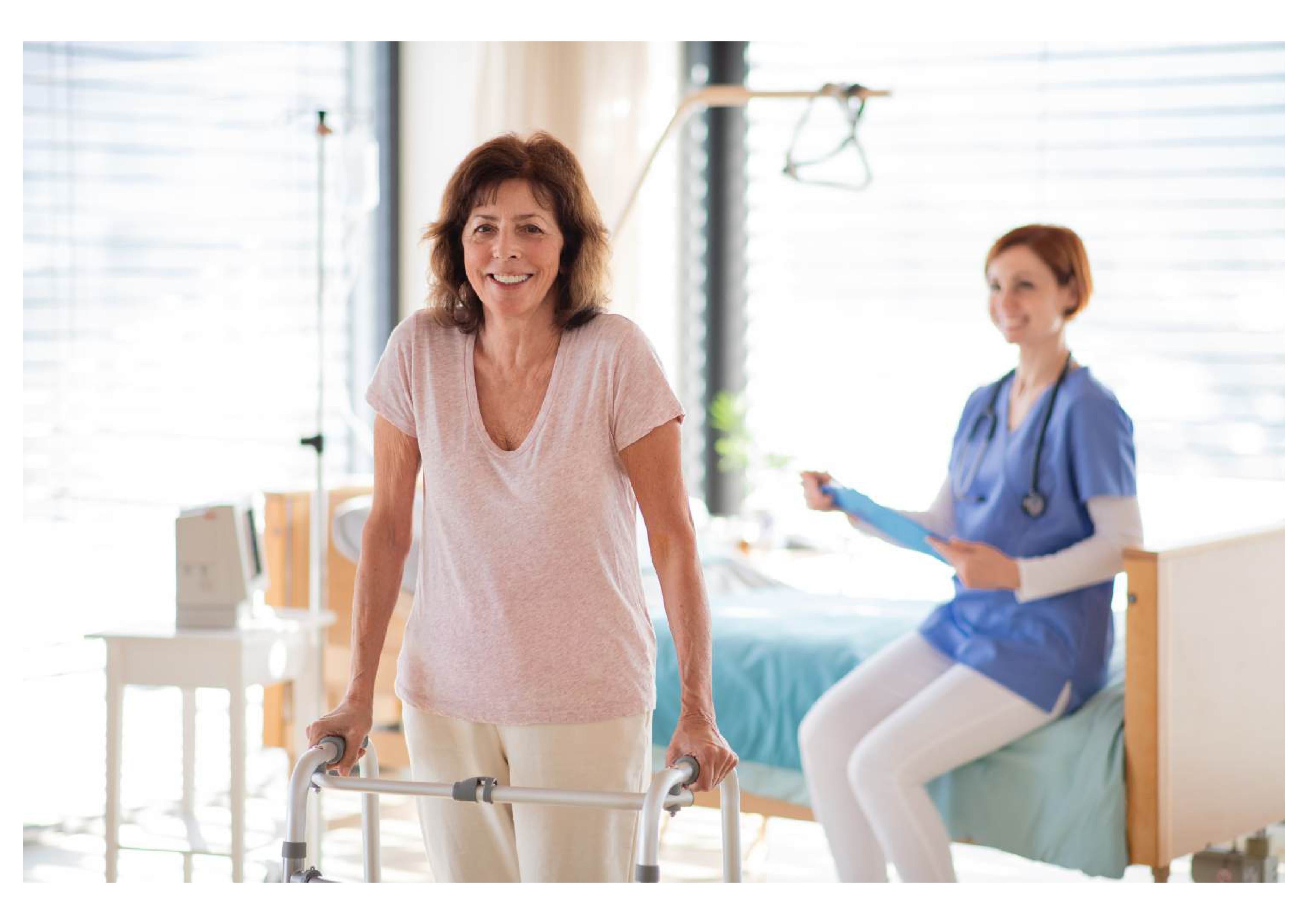 Patient mobility training: woman using a walker in a hospital room under nurse supervision for recovery.