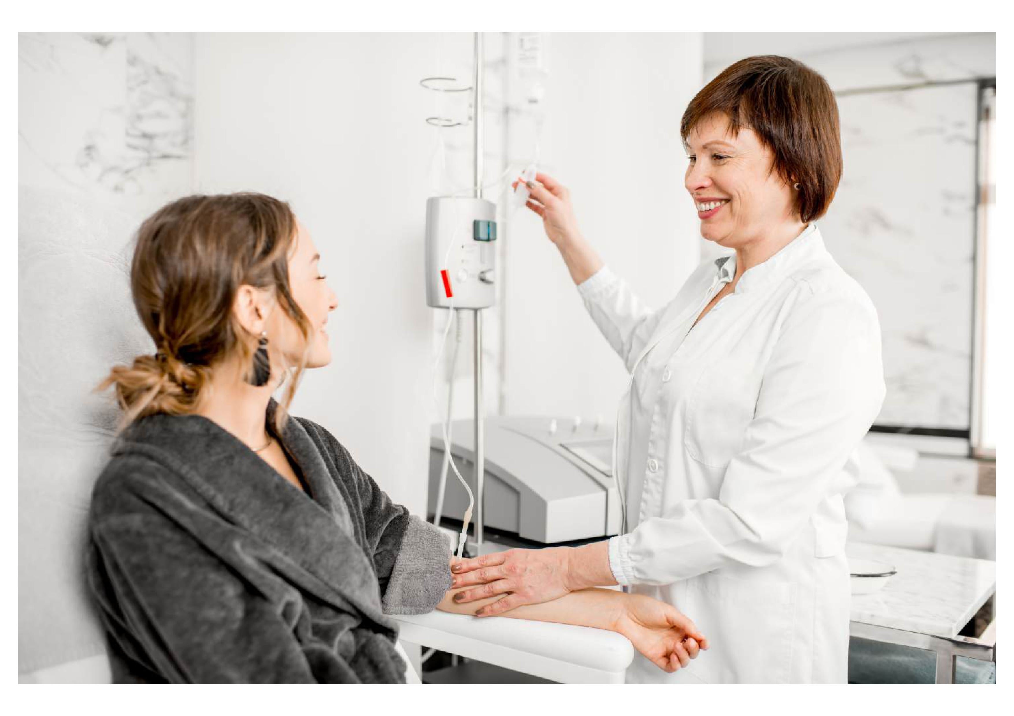 Nurse’s hand adjusting IV drip chamber and tubing in a hospital room, with IV fluid bags and manual drip system