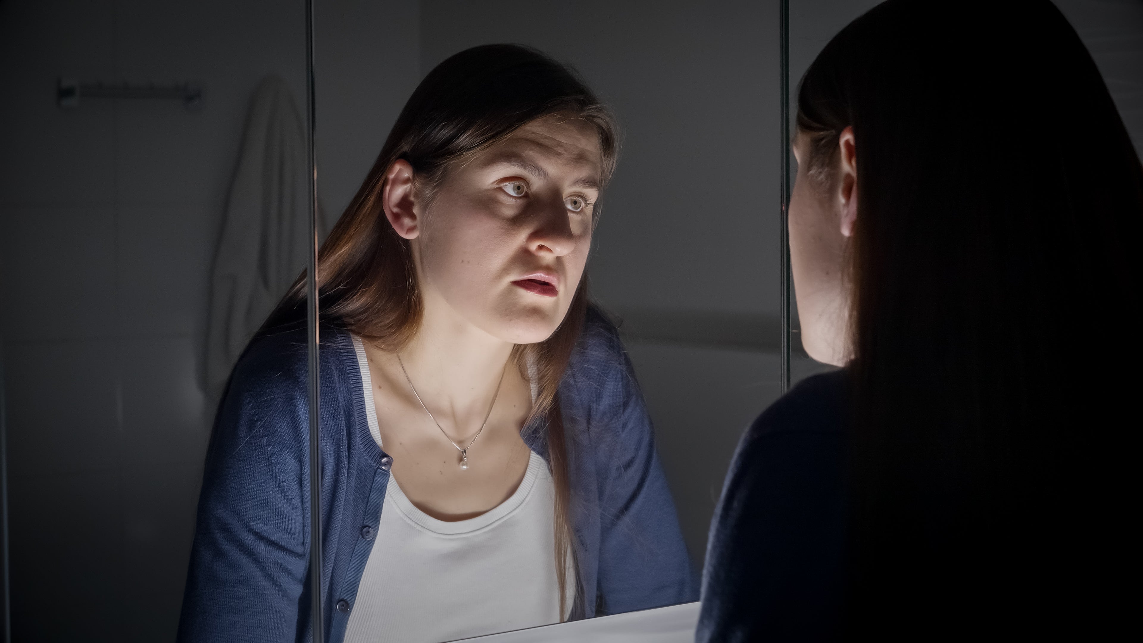 Unhappy expression on woman's face as they view themselves in the mirror, indicating emotional distress